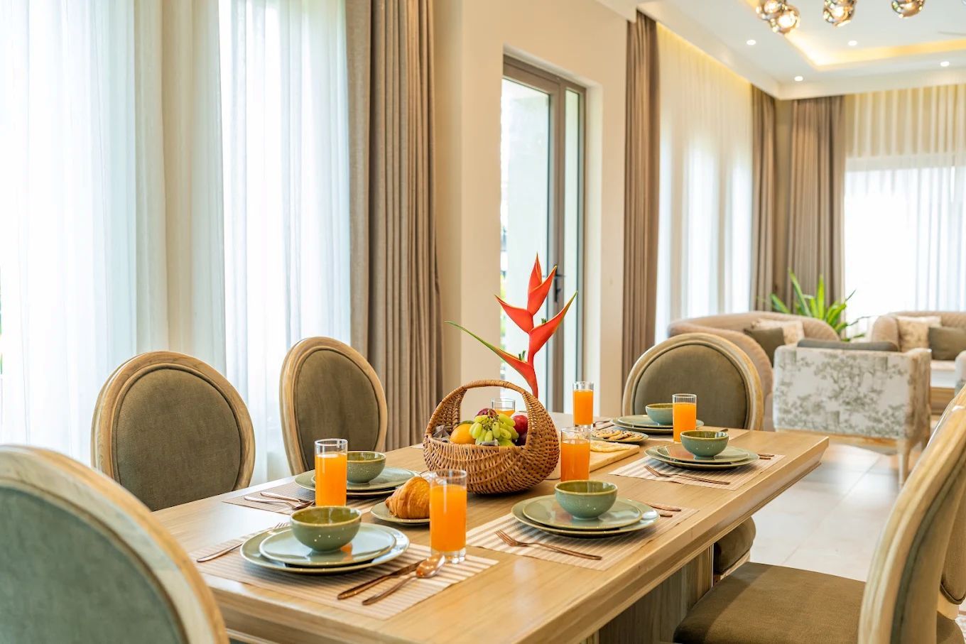 A dining area with a long table set for breakfast, including plates, bowls, and glasses of orange juice.