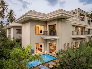 A multi-story hotel with a swimming pool, balconies, and lush greenery. - Paddy Field View 5 Mins Drive to Beach  (Goa)