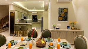 Uma sala de jantar moderna com uma mesa posta para quatro pessoas, uma cozinha ao fundo e uma escada que leva a outro andar.