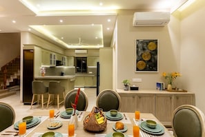 A modern dining area with a table set for four, a kitchen in the background, and a staircase leading to another level. - Paddy Field View 5 Mins Drive to Beach  (Goa)