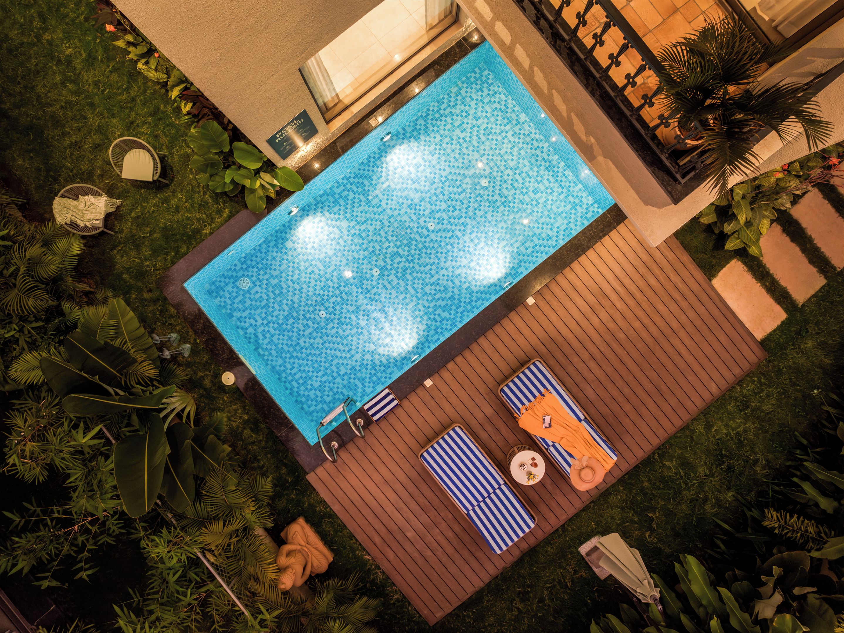 A rooftop pool with a tiled surface, surrounded by lush greenery and wooden decking.