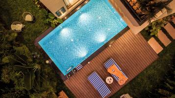 A rooftop pool with a tiled surface, surrounded by lush greenery and wooden decking.