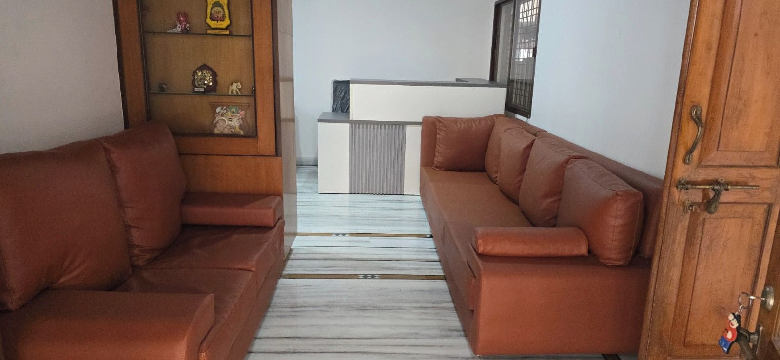 Una sala de estar con dos sofás marrones, un aparador de madera con adornos y una consola blanca.