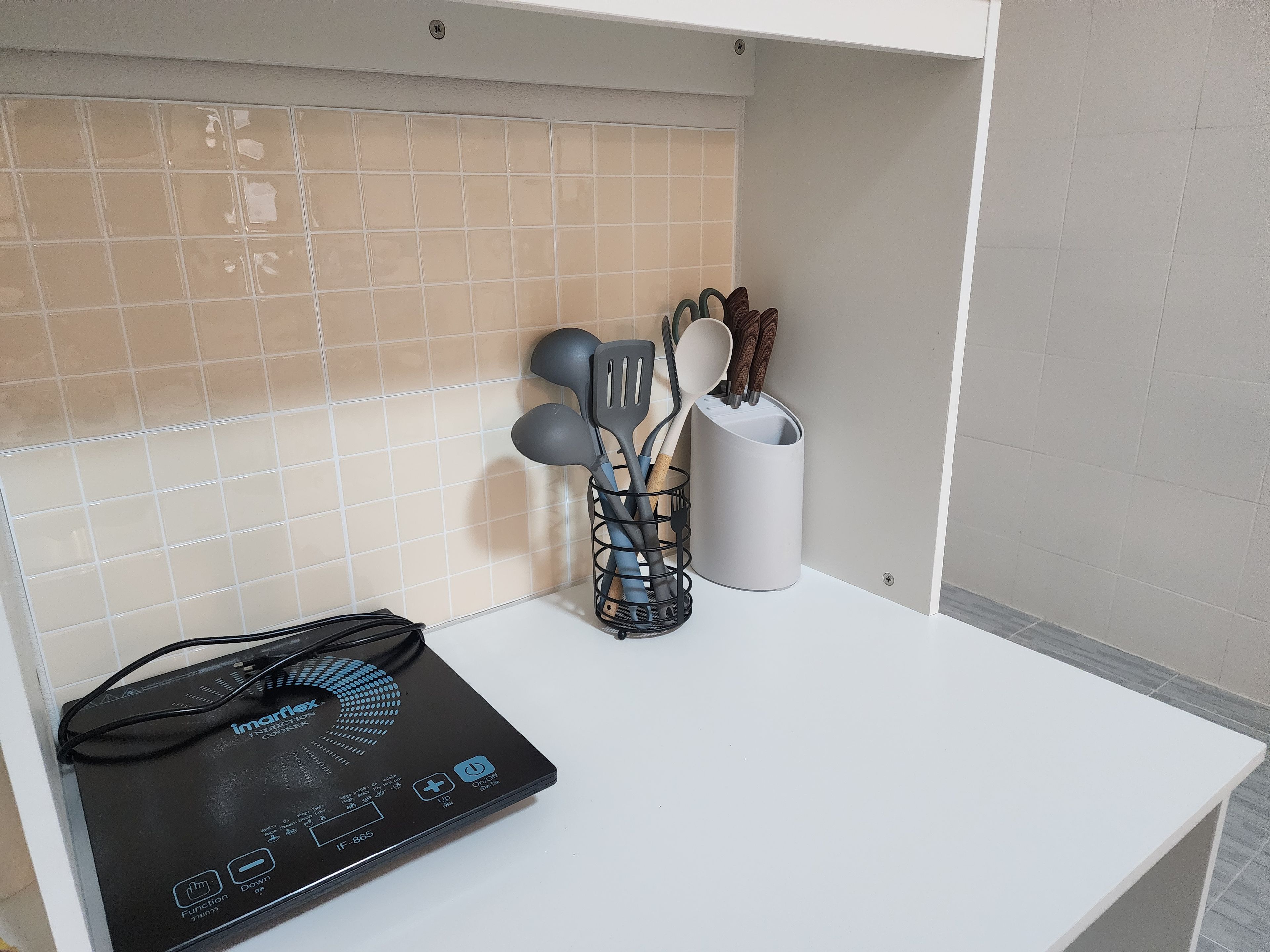 A kitchen with a white countertop, a black induction cooktop, and a utensil holder with spatulas and spoons.