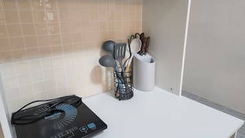 A kitchen with a white countertop, a black induction cooktop, and a utensil holder with spatulas and spoons.