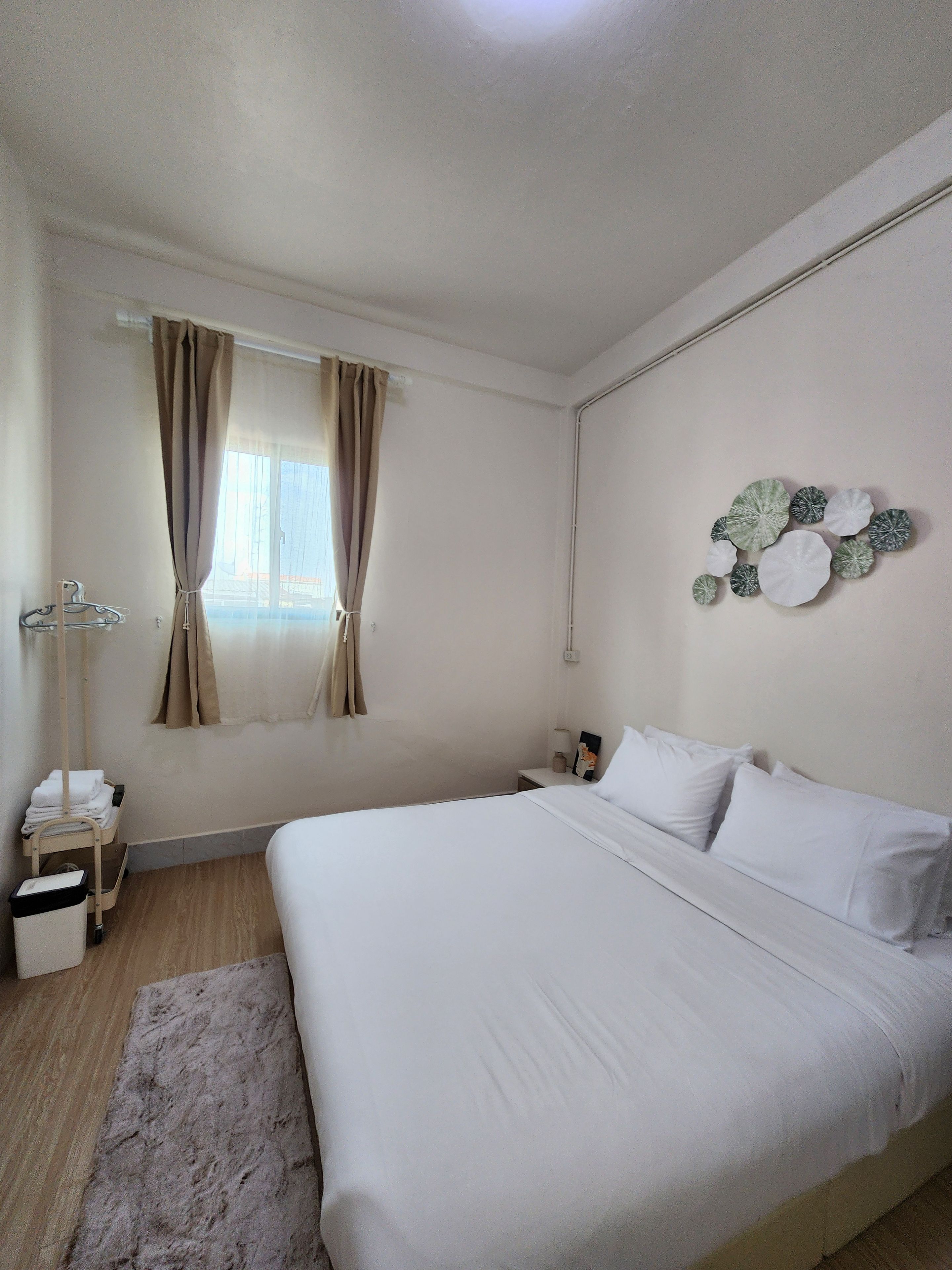 A hotel room with a large bed, a bedside table with a lamp, a wall-mounted artwork, and a window with curtains.