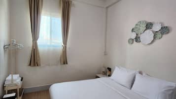 A hotel room with a large bed, a bedside table with a lamp, a wall-mounted artwork, and a window with curtains.
