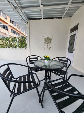 Een overdekt terras met een ronde tafel en vier stoelen.