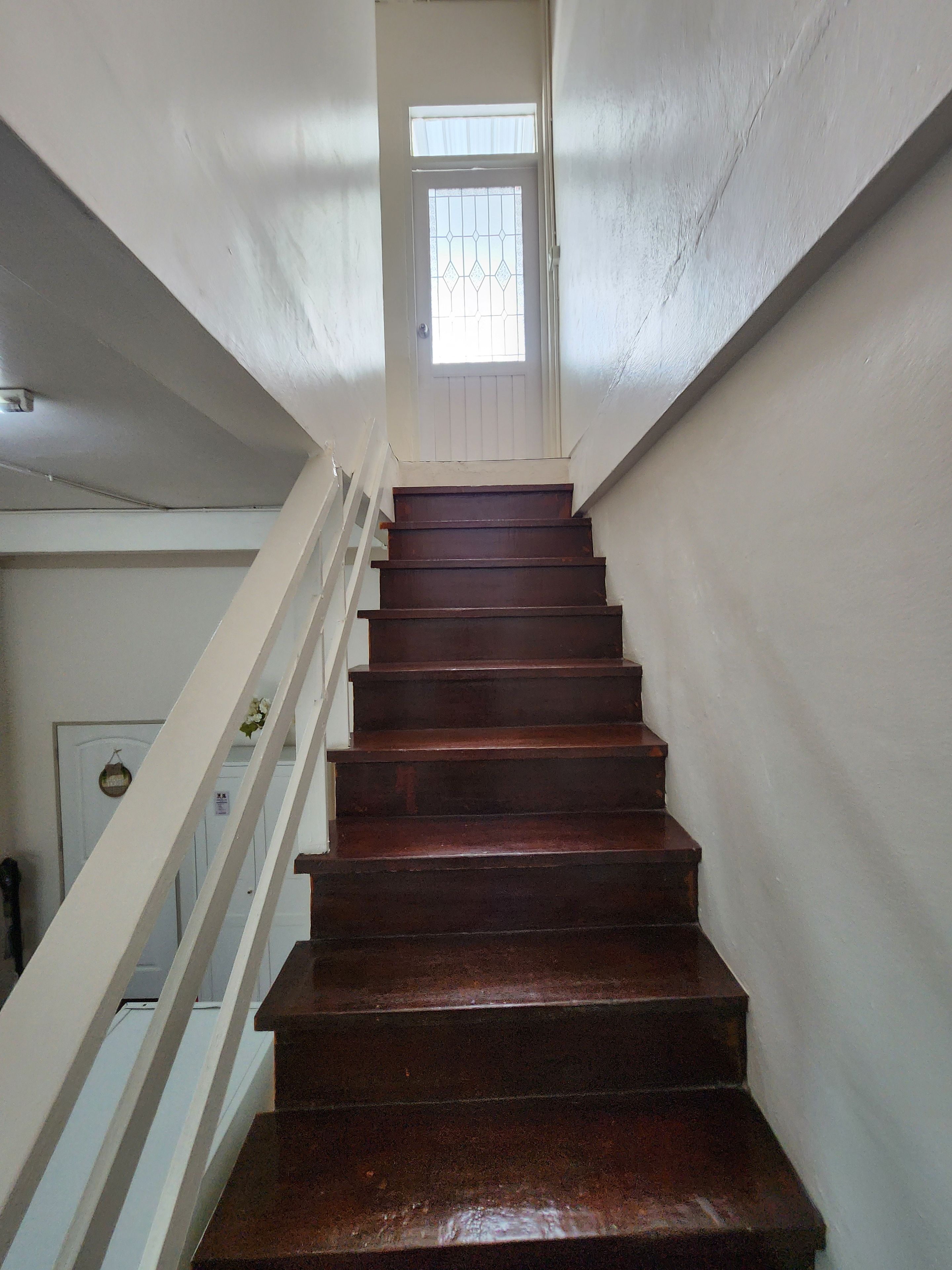 A wooden staircase with white railings leading to a door with a window.