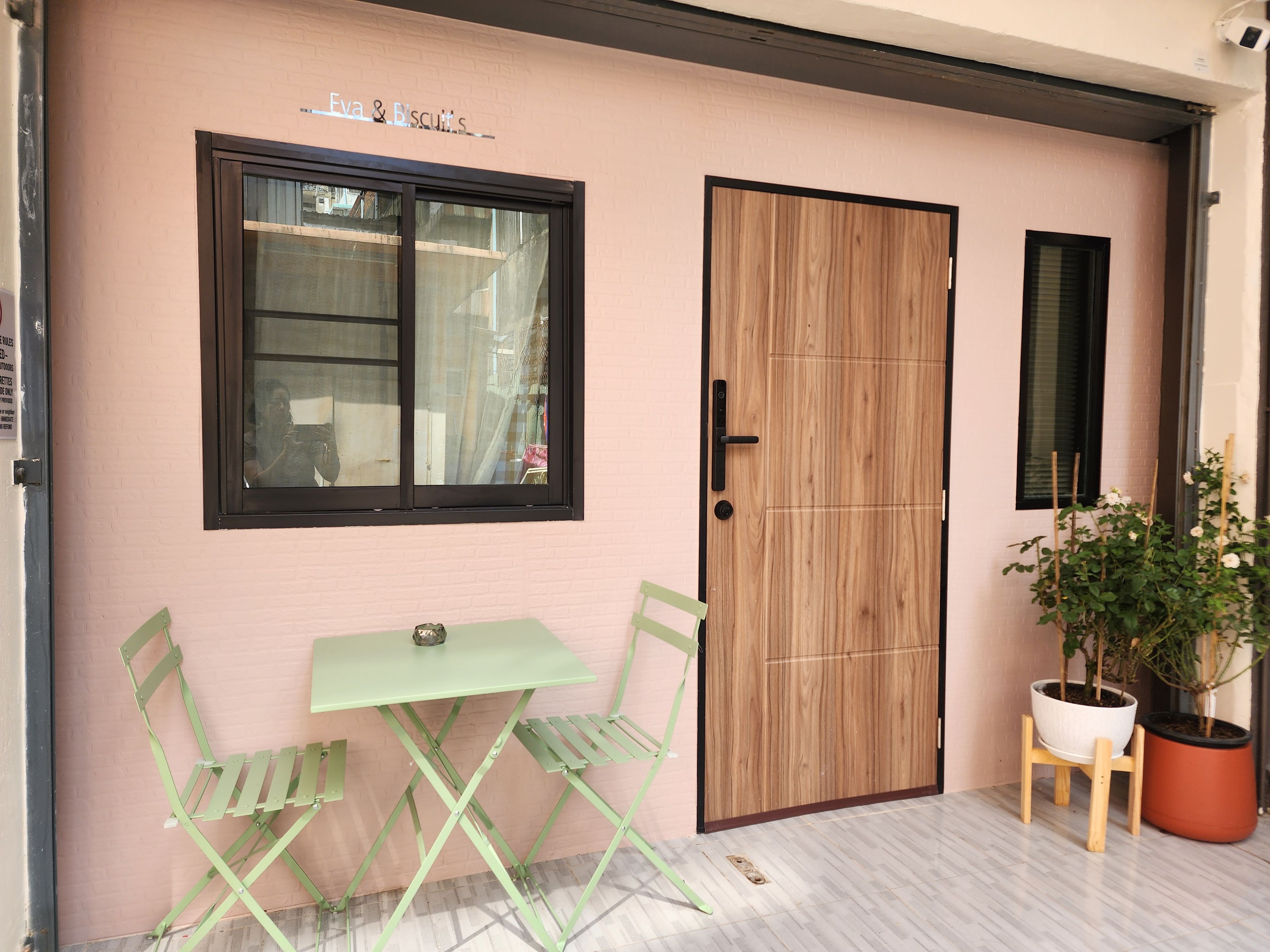 Una pared de ladrillo rosa con una puerta de madera, una ventana y una mesa plegable verde con sillas.