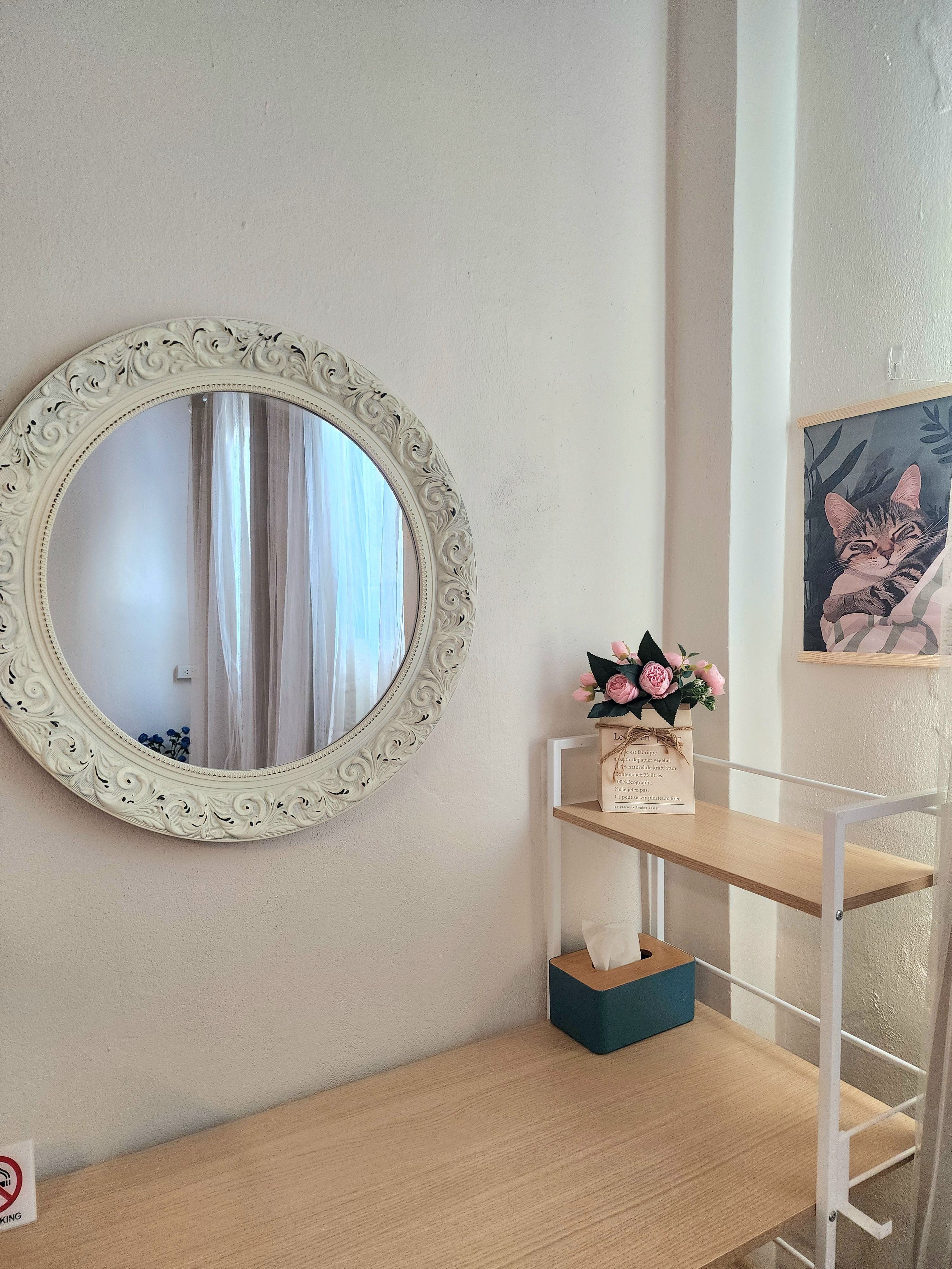 A mirror with an ornate frame, a wooden shelf with a tissue box, and a framed picture on the wall.