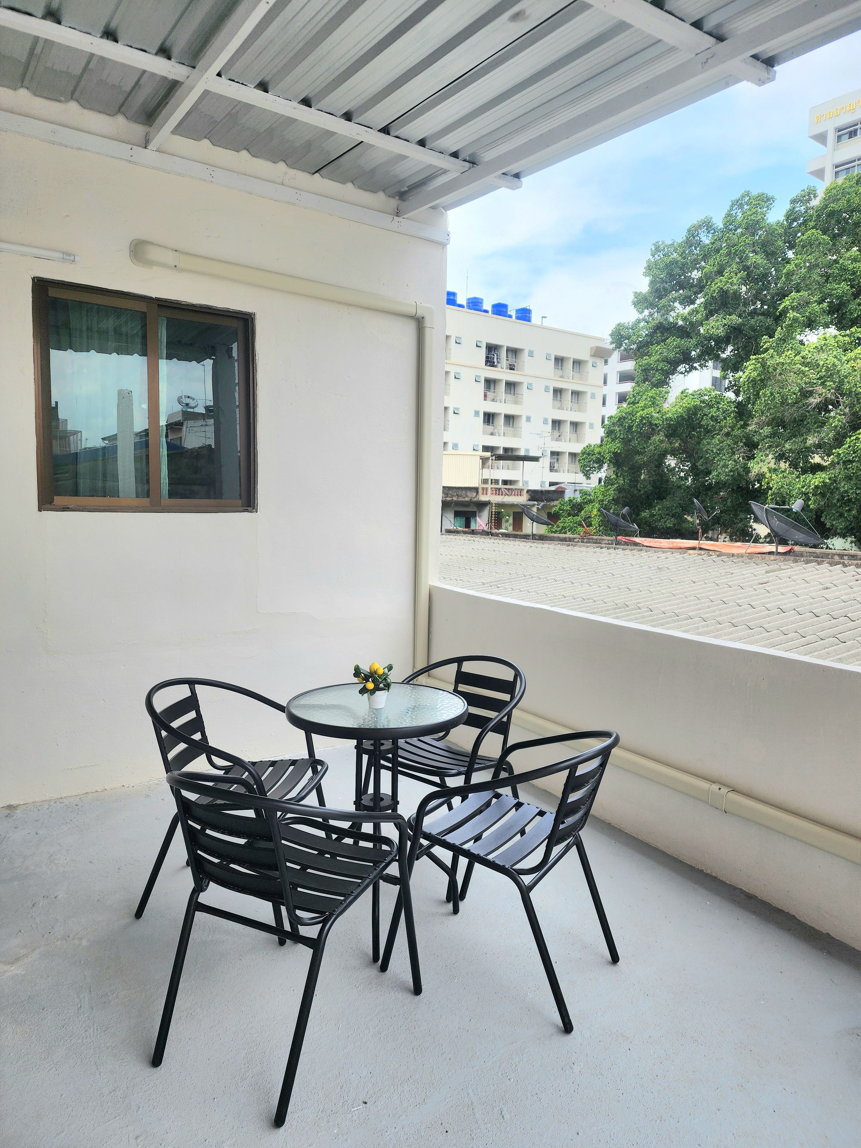 A balcony with a table and chairs, a window, and a view of a building and trees.