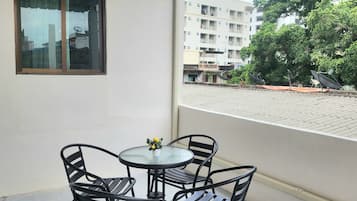 A balcony with a table and chairs, a window, and a view of a building and trees.