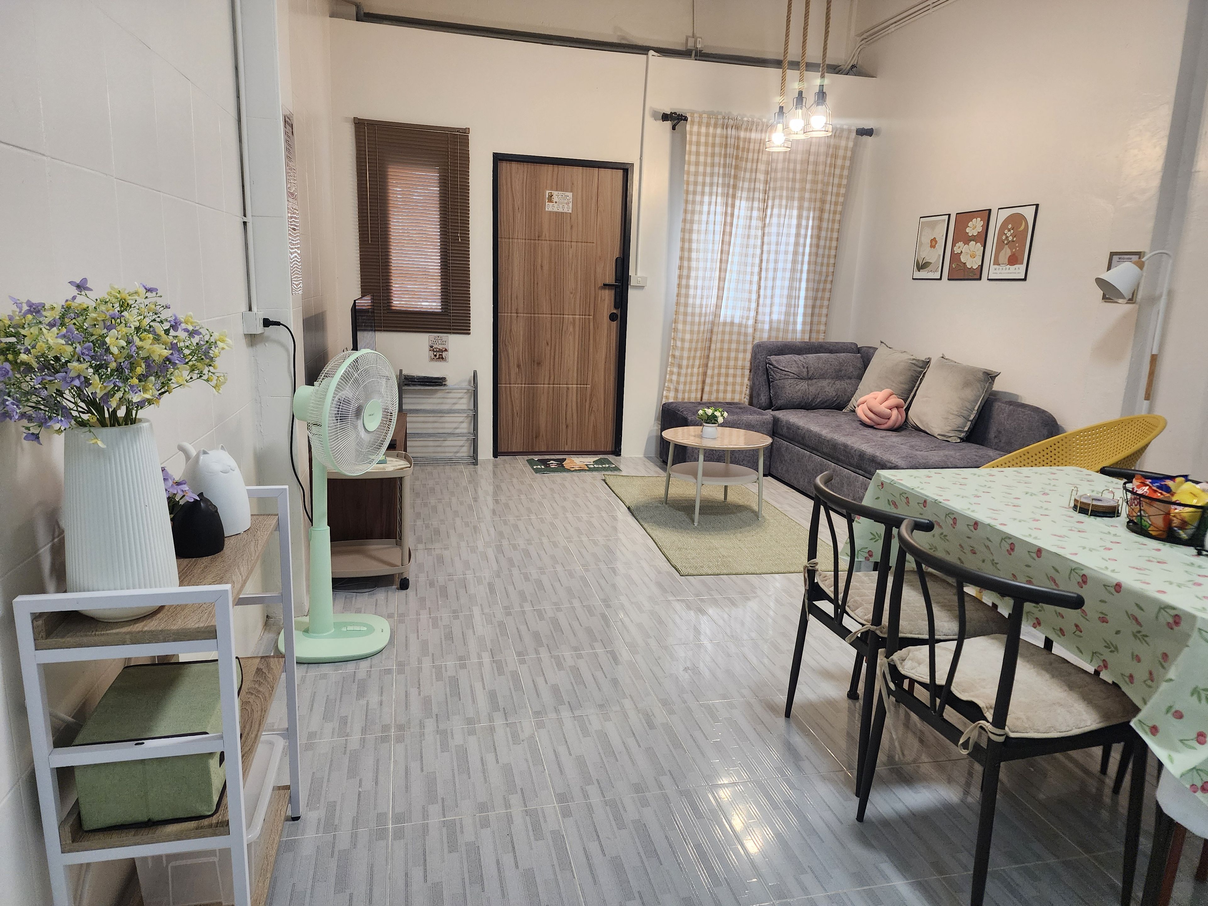 A compact living space with a sofa, a dining table, a fan, and a small table with a vase of flowers.