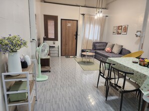 A compact living space with a sofa, a dining table, a fan, and a small table with a vase of flowers. - 2BR 3-Story Home, Walk to BTS and Sathorn Pier, Free Netflix (Yan Nawa, Sathon)