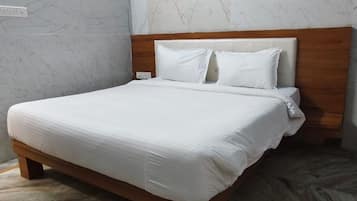Una cama bien tendida con cabecera de madera, ropa blanca y una pared con diseño de mármol.
