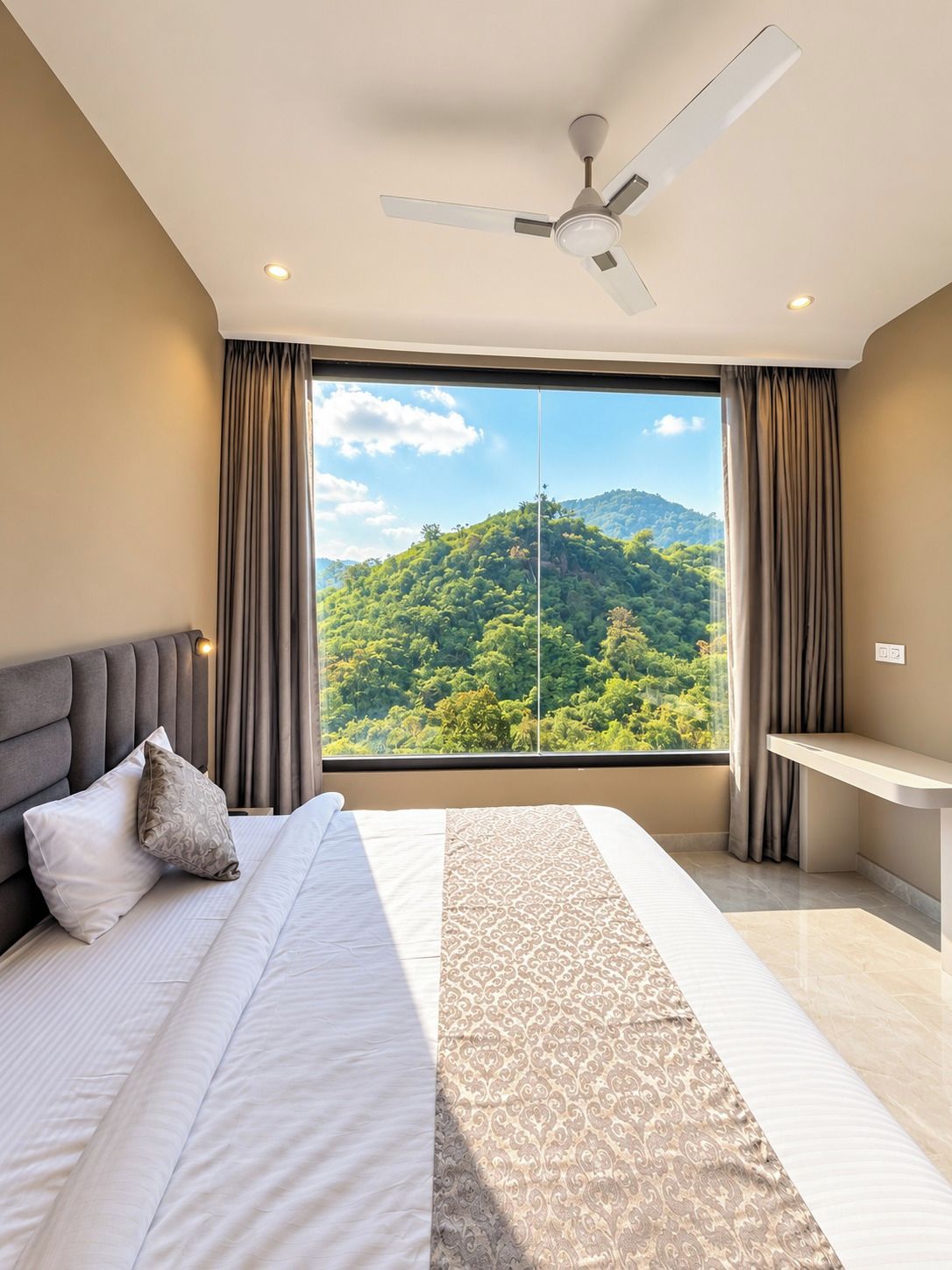 Une chambre à coucher comprenant un lit, un bureau, un ventilateur de plafond et une grande fenêtre donnant sur la montagne.