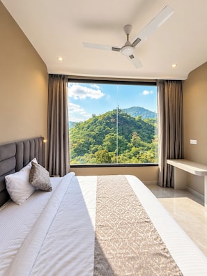 Une chambre à coucher comprenant un lit, un bureau, un ventilateur de plafond et une grande fenêtre donnant sur la montagne.