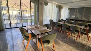 Un espace repas avec des tables et des chaises, de grandes fenêtres avec des rideaux et une vue sur une étendue d’eau.