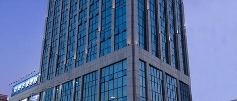 A modern hotel building with a glass facade, multiple floors, and a prominent signage at the top.