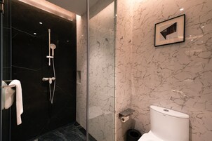 A modern bathroom with a glass-enclosed shower, marble walls, a toilet, and a framed picture on the wall.