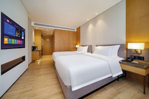 A hotel room with a large bed, bedside tables, a desk, and a television displaying a menu.