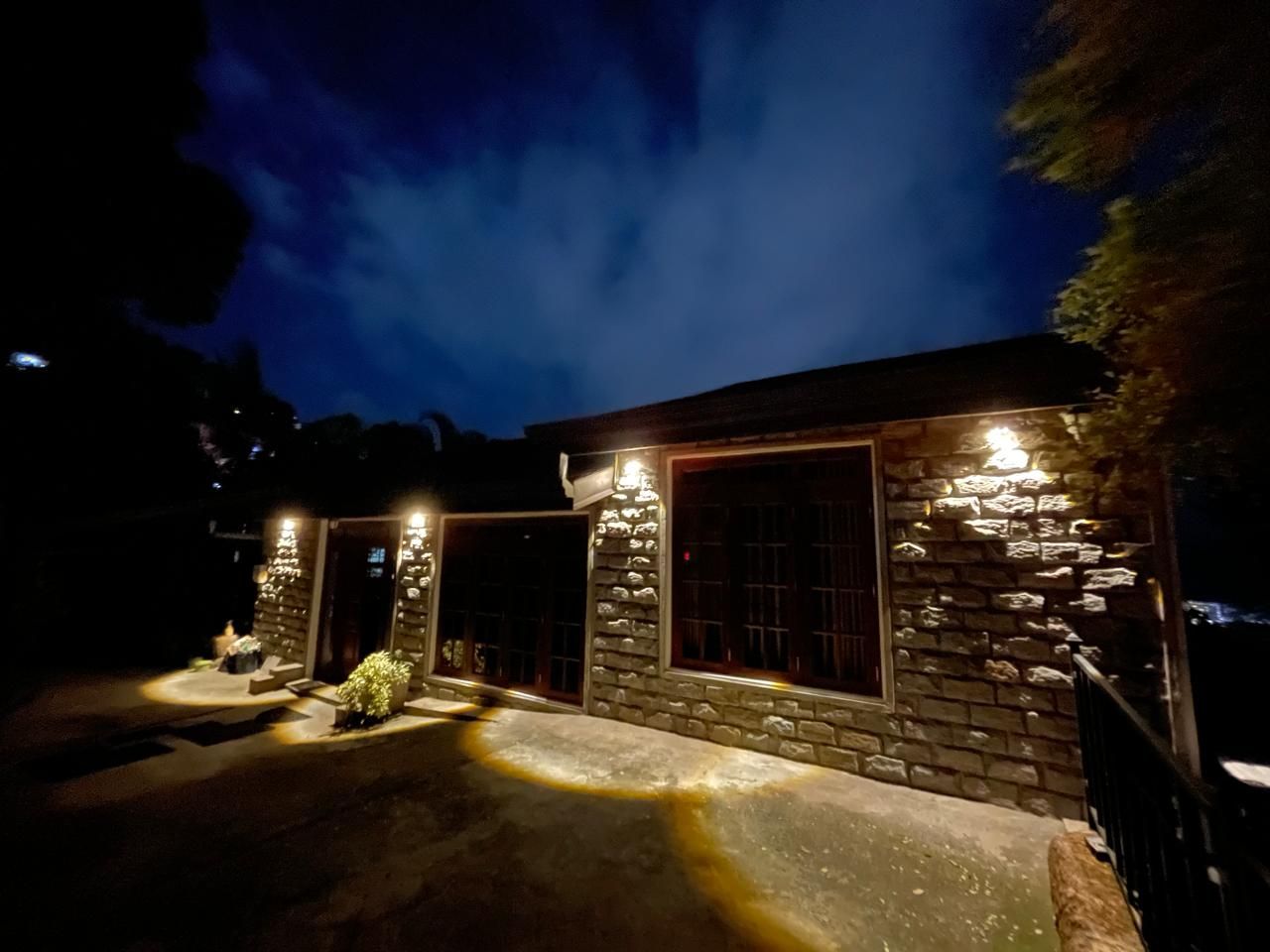 A stone building with illuminated windows and a paved entrance area.