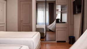 Hotellihuone, jossa on sänky, peili, televisio ja kahvinkeitin.