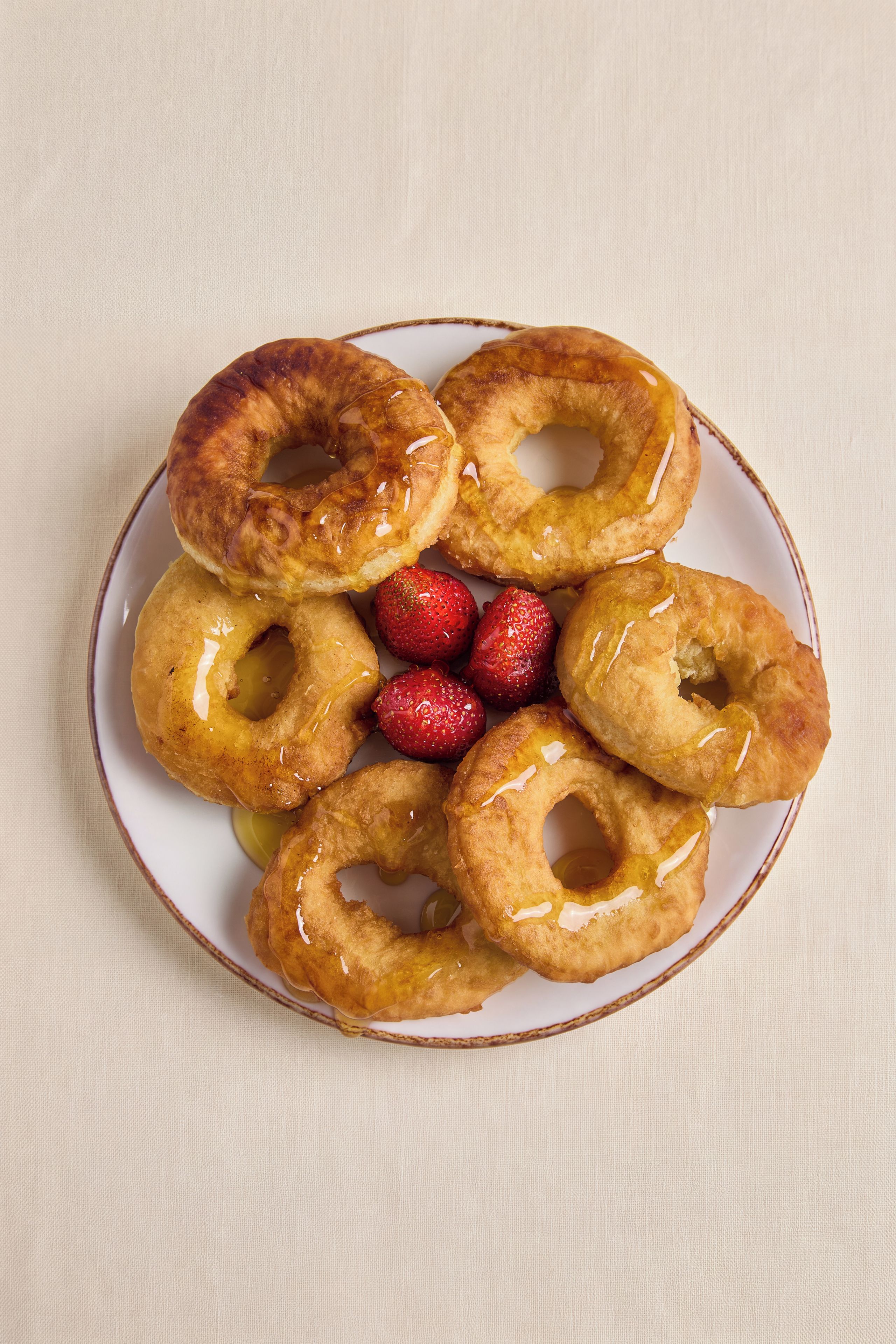 Een bord met glazuurbelegde donuts en aardbeien.
