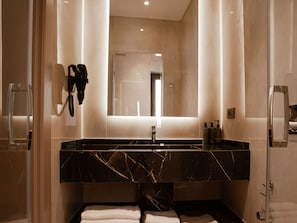 Une salle de bain moderne avec un lavabo en marbre, un grand miroir et une douche à parois de verre.