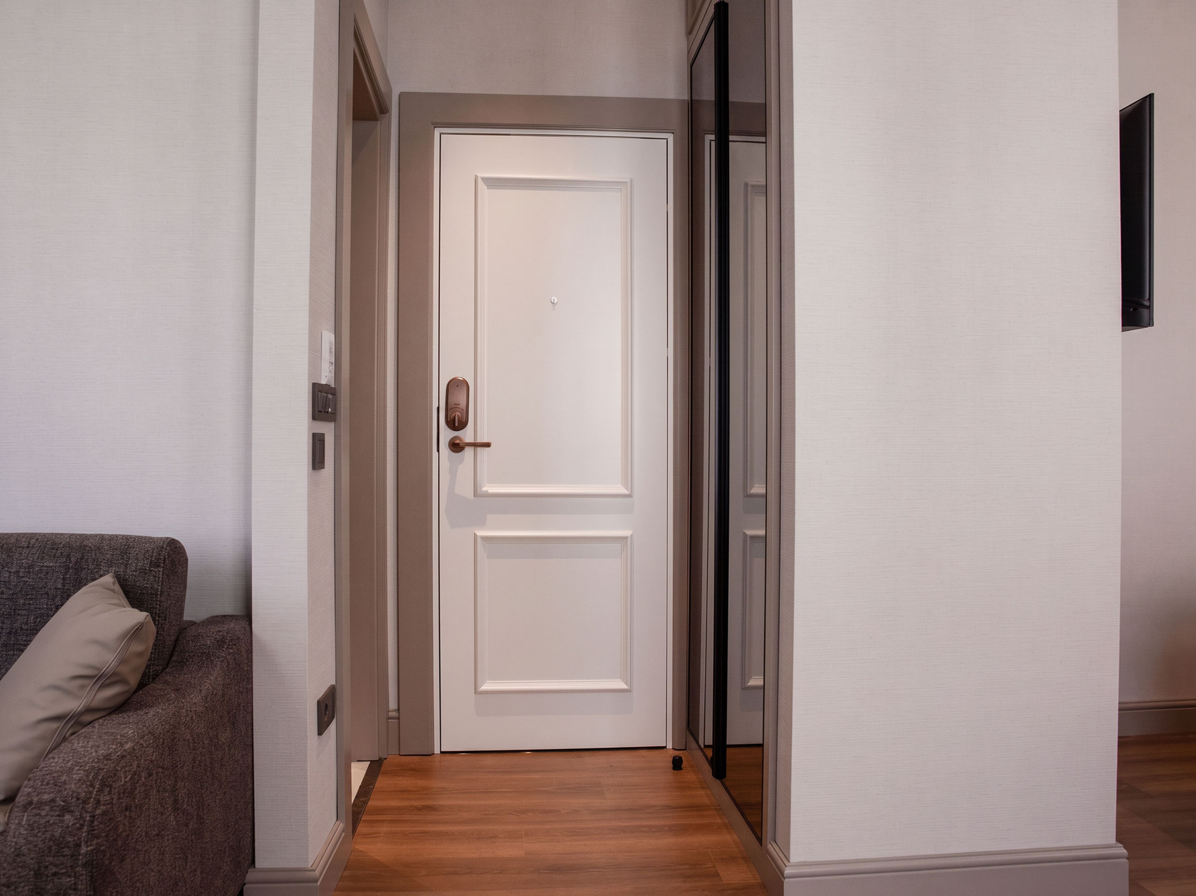 A hallway with a closed white door, a grey sofa with a cushion, and a wooden floor.