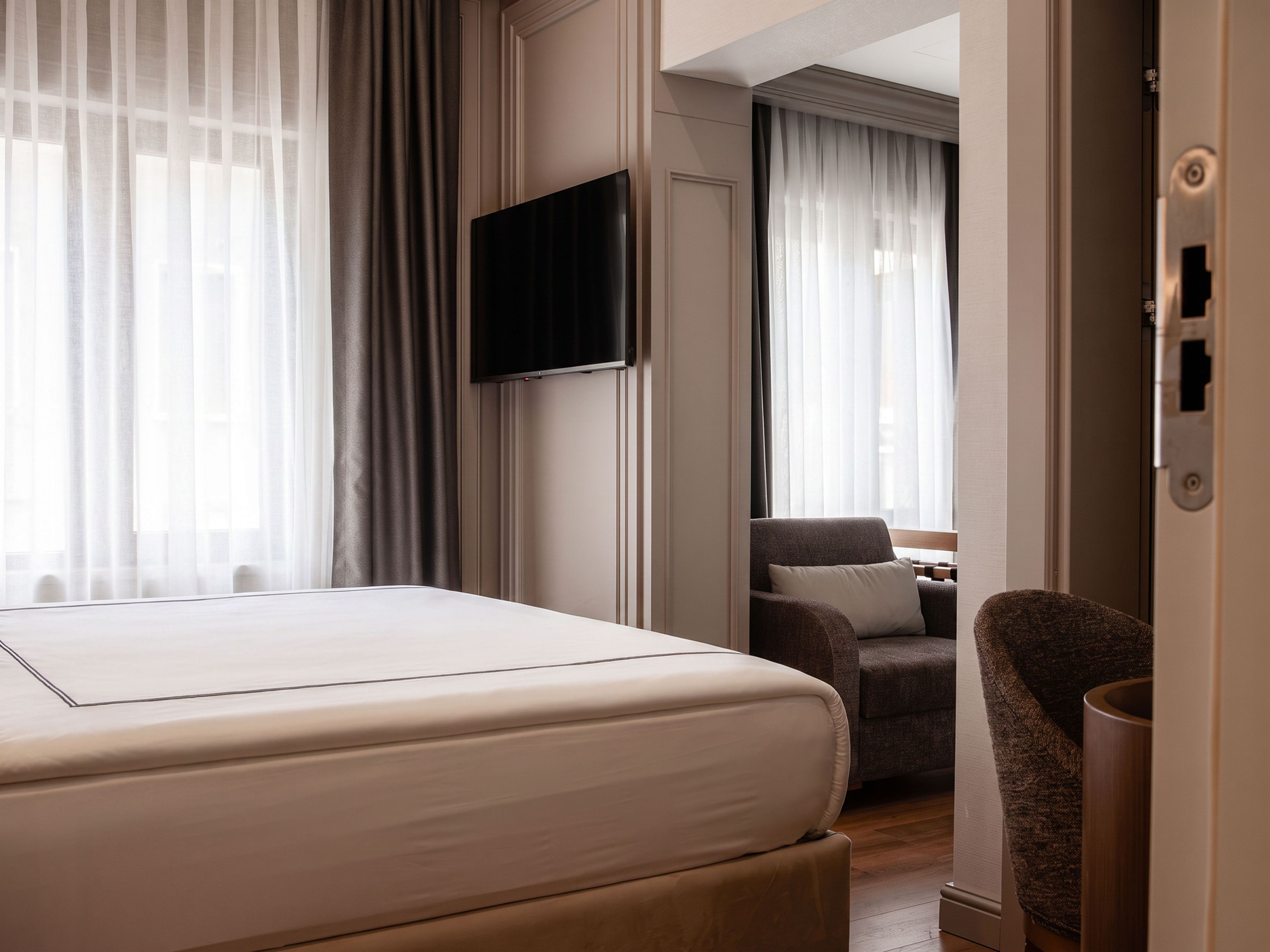 Habitación de hotel con cama, televisor montado en la pared, una silla y una puerta con cerradura.