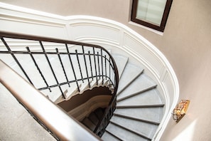 Una escalera de caracol con barandilla de metal, escalones alfombrados y una lámpara fijada a la pared.