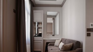 Moderni hotellihuone, jossa on sohva, peili, pieni keittiö ja puulattia.