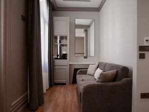 Une chambre d’hôtel moderne avec un canapé, un miroir, une kitchenette et un plancher en bois.