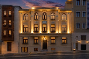 Un edificio de varios pisos con fachada simétrica, que presenta una entrada central con puerta oscura, flanqueada por ventanas con detalles decorativos y un reloj encima.