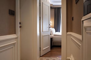Un pasillo que conduce a un dormitorio con cama, una puerta y una lámpara fijada a la pared.