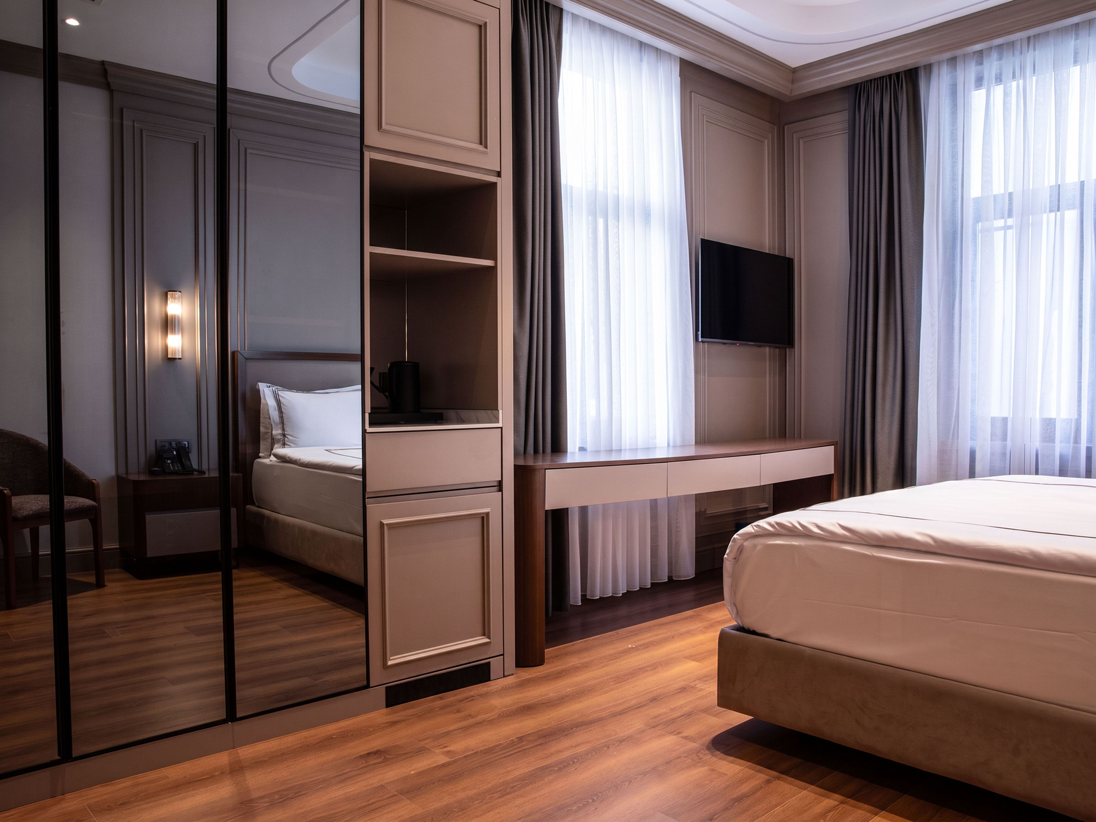 A hotel room with a bed, a desk, a chair, a television, and a mirror.