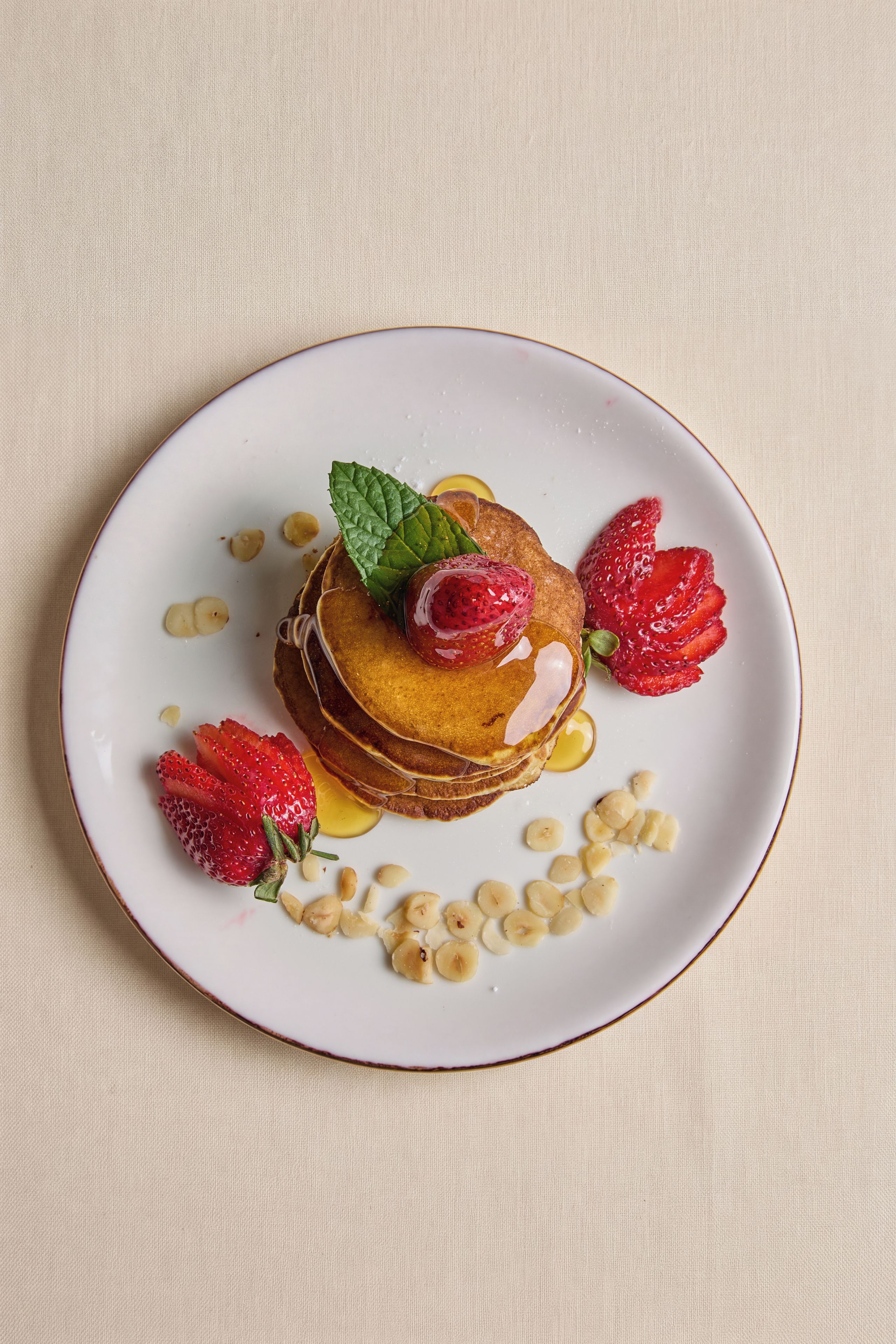 A plate of pancakes with strawberries and a mint leaf on a textured surface.