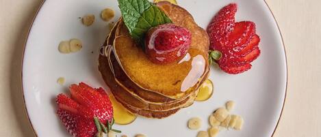 A plate of pancakes with strawberries and a mint leaf on a textured surface.