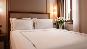 Hotellihuone, jossa on suuri sänky, yöpöytä, maljakko kukkineen ja ikkuna, jossa on verhot.