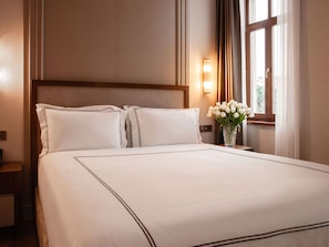 Une chambre d’hôtel avec un grand lit, une table de chevet, un vase de fleurs et une fenêtre avec des rideaux.