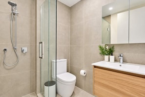 Un baño moderno con cabina de ducha de vidrio, inodoro, lavamanos con espejo y planta en maceta.