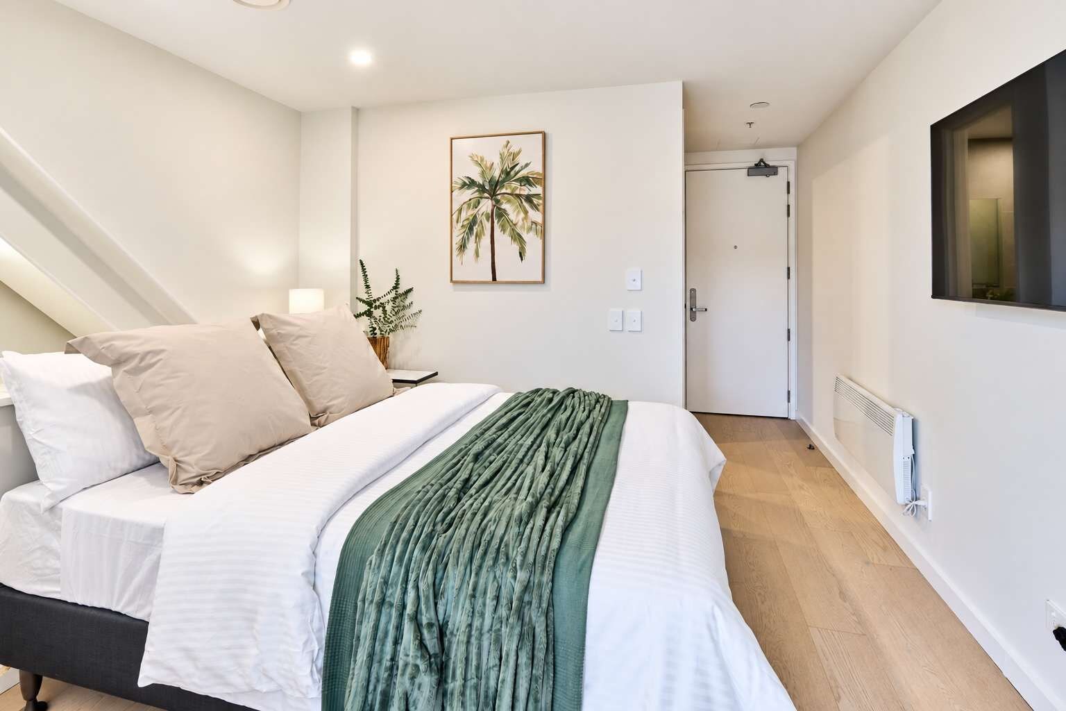 Quarto com cama, almofadas, manta verde, quadro na parede, porta e radiador.