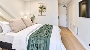 Quarto com cama, almofadas, manta verde, quadro na parede, porta e radiador.