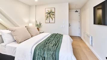 Quarto com cama, almofadas, manta verde, quadro na parede, porta e radiador.