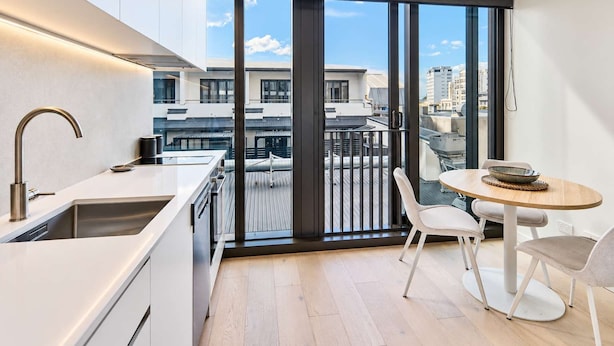 Cozinha moderna com uma janela ampla, área de jantar com mesa e cadeiras, e vista para a paisagem urbana.