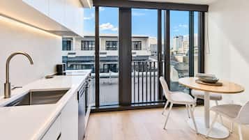 Cozinha moderna com uma janela ampla, área de jantar com mesa e cadeiras, e vista para a paisagem urbana.