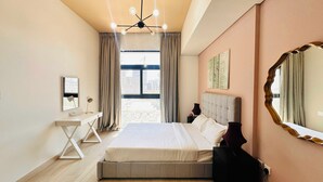 Quarto de hotel com uma cama grande, escrivaninha, cadeira, espelho e vista para a paisagem urbana.