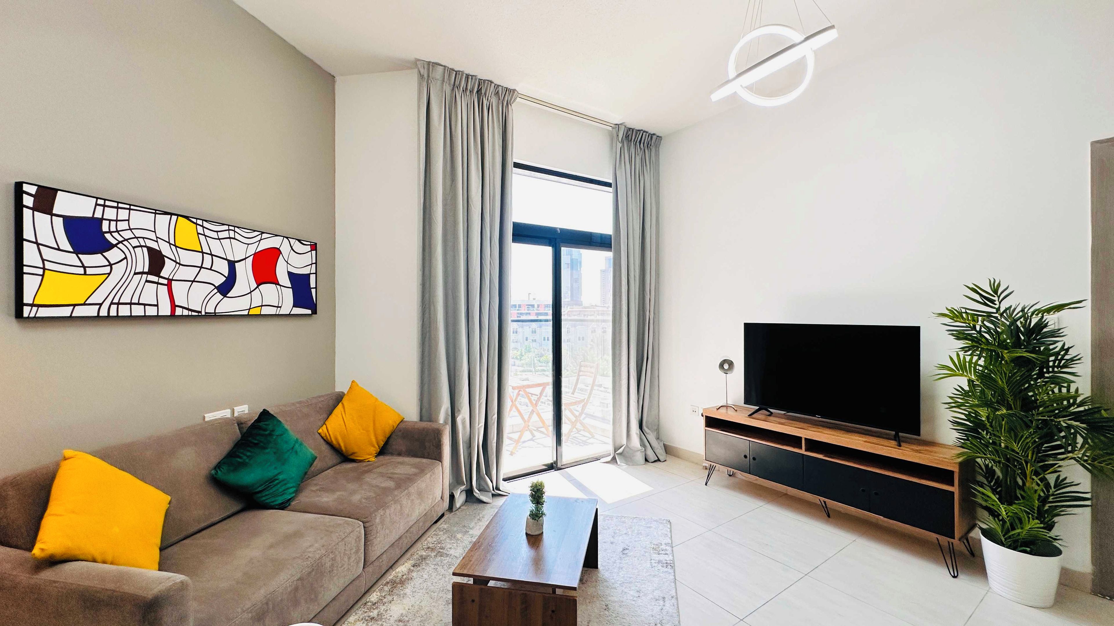 A modern living room with a sofa, a coffee table, a flat-screen TV, a potted plant, and a large window with curtains.